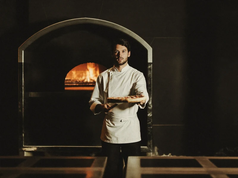 Four à bois incandescent et pizzaiolo enfournant une pizza dans une salle sombre