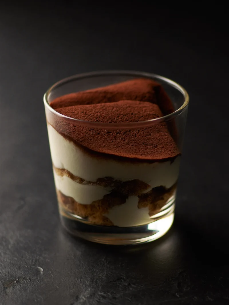 Tiramisu en verrine saupoudré de cacao sur un comptoir en pierre sombre